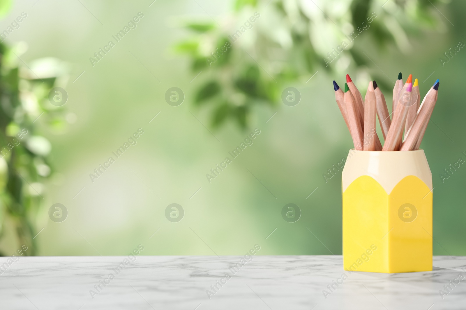 Photo of Colorful pencils in holder on white marble table. Space for text