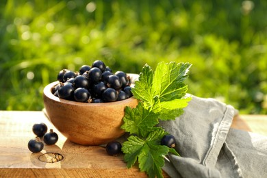 Ripe blackcurrants in bowl and leaves on wooden surface outdoors. Space for text