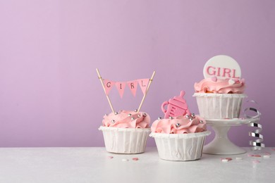Photo of Baby shower cupcakes with pink cream and toppers on white table against violet background
