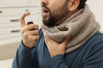 Photo of Young man with scarf using throat spray indoors, closeup