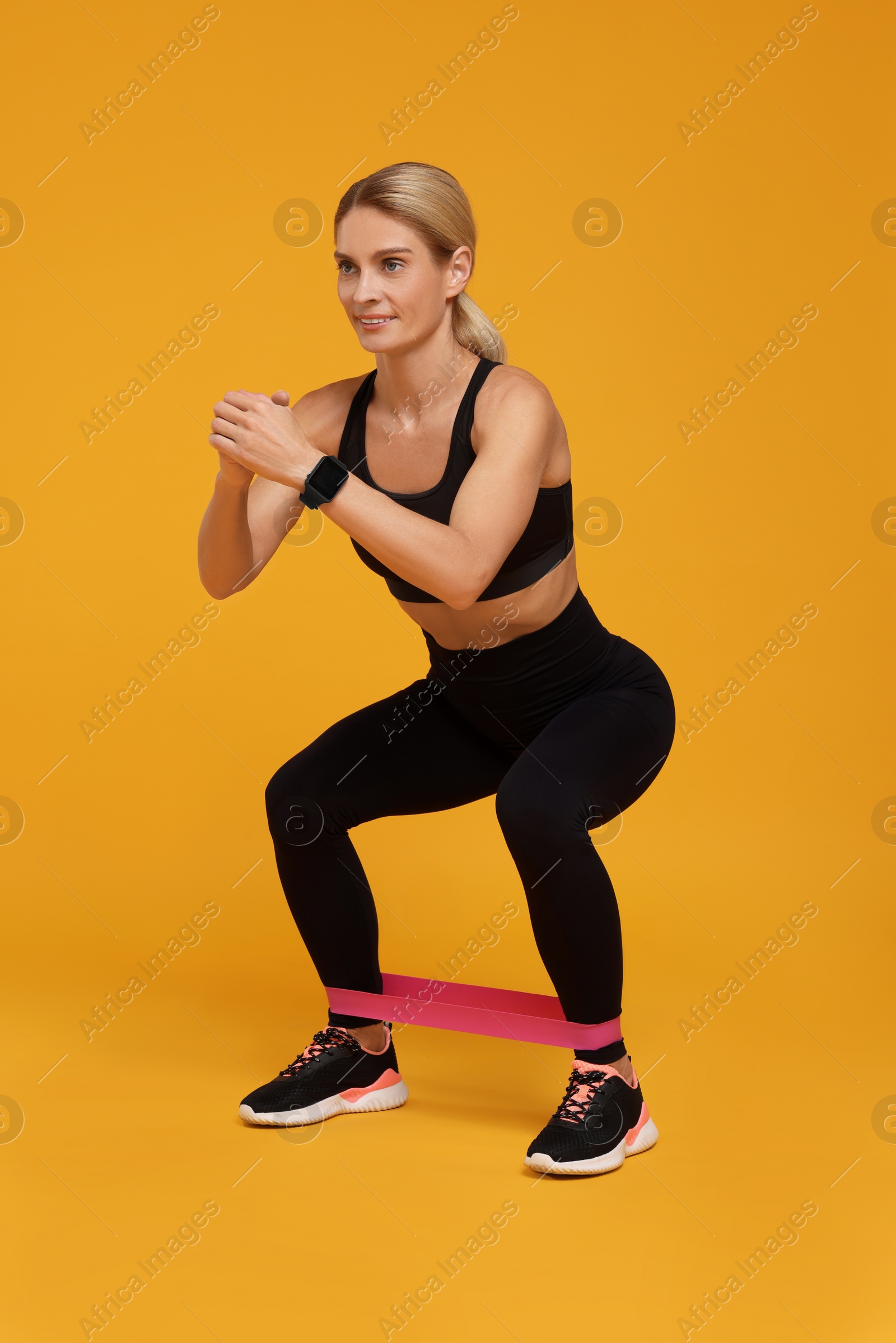 Photo of Woman exercising with elastic resistance band on orange background