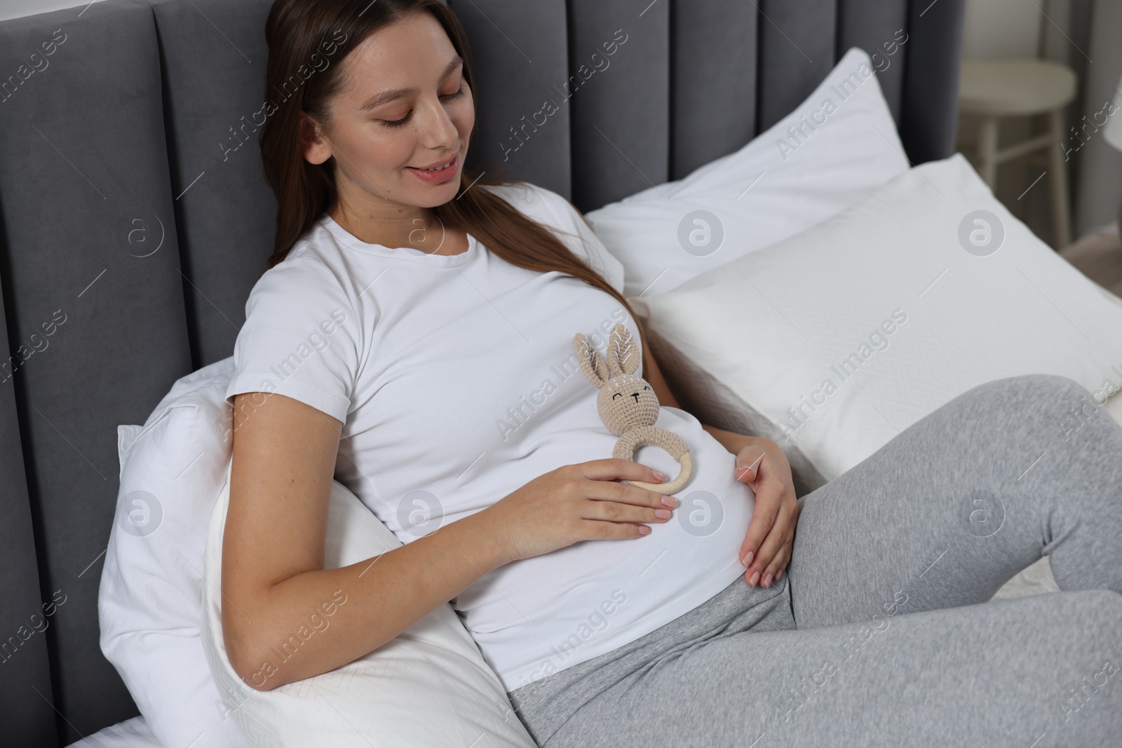 Photo of Beautiful pregnant woman with bunny toy on bed indoors