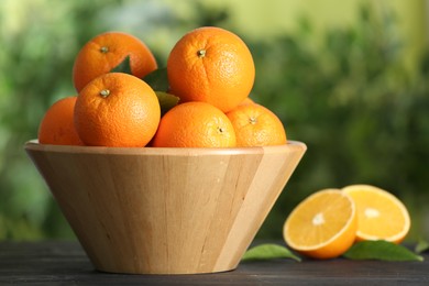 Photo of Fresh ripe oranges in bowl on wooden table against blurred background