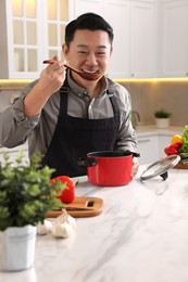 Cooking process. Man tasting dish at countertop in kitchen