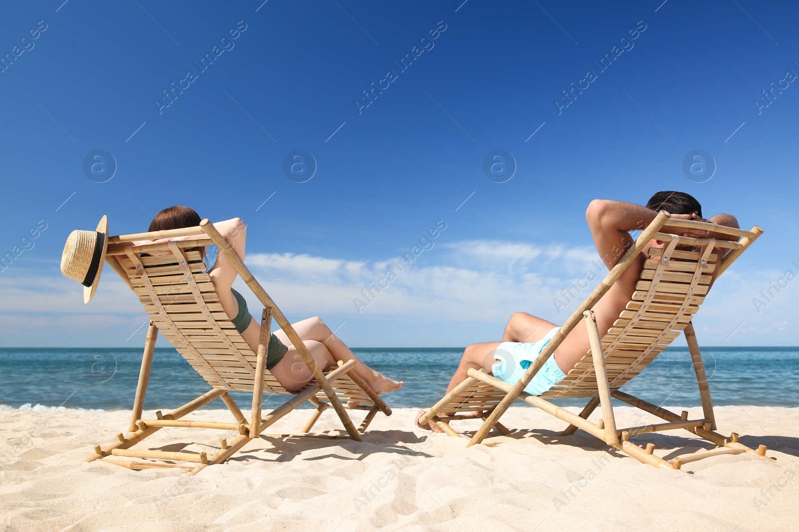 Photo of Woman in bikini and her boyfriend on deck chairs at beach. Lovely couple