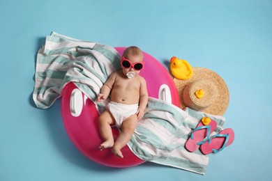 Cute little baby in sunglasses with inflatable ring and beach accessories on light blue background, top view