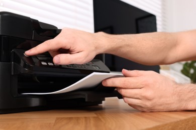 Photo of Man using modern printer at wooden table indoors, closeup