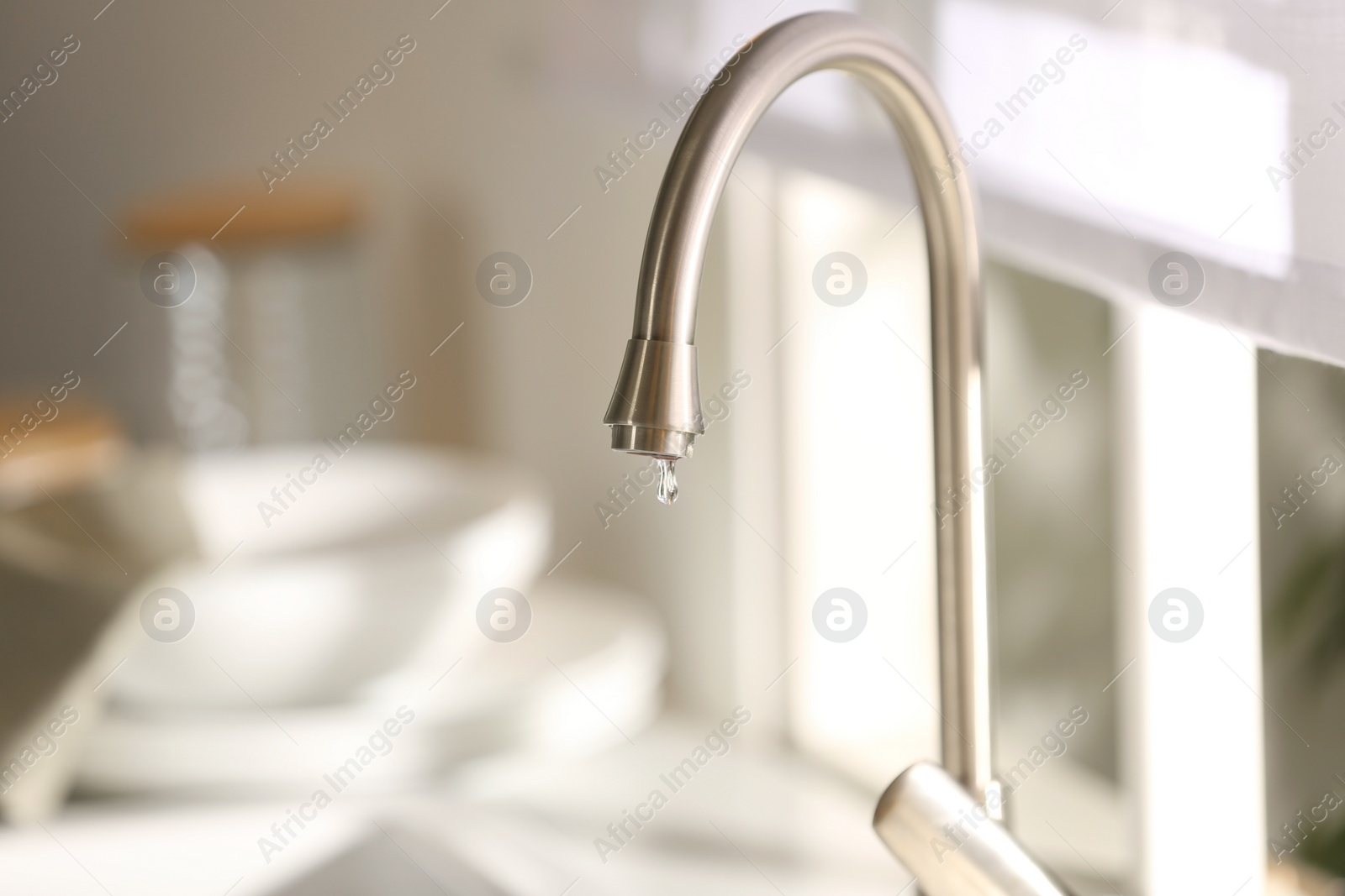 Photo of Water drop falling down from tap on blurred background, closeup