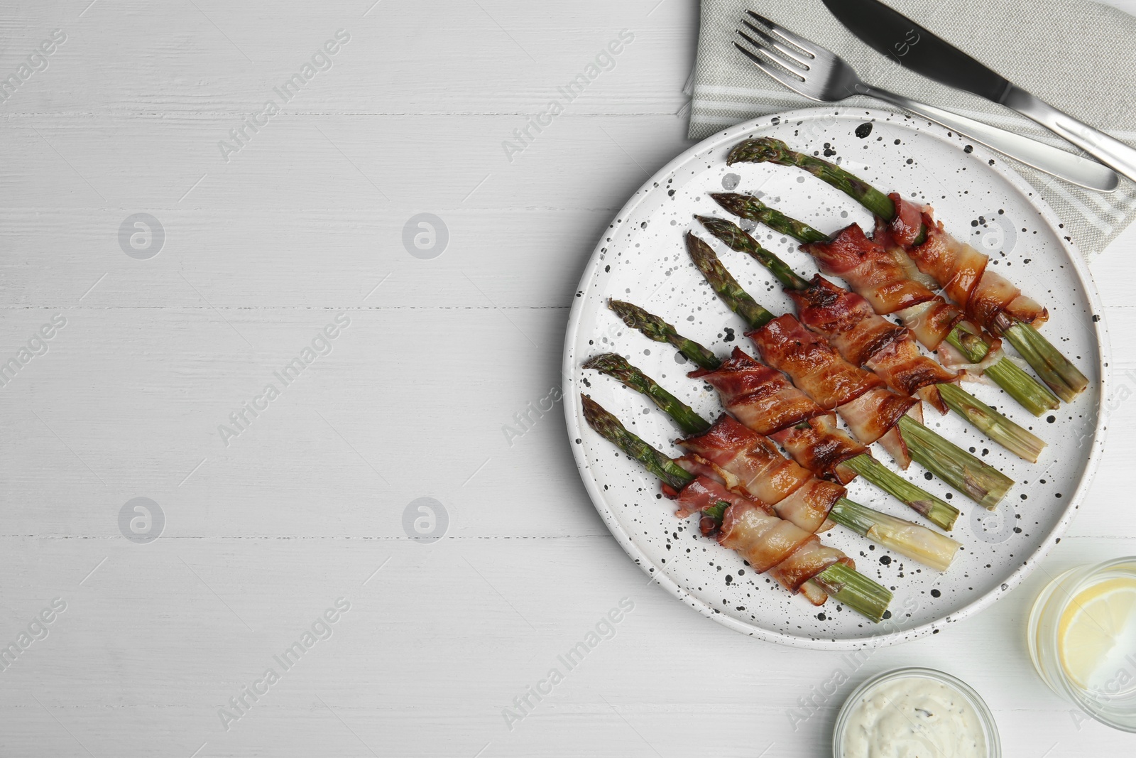 Photo of Oven baked asparagus wrapped with bacon on white wooden table, flat lay. Space for text