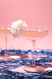 Tasty cocktail in glass decorated with cotton candy and blue shiny streamers on pink background