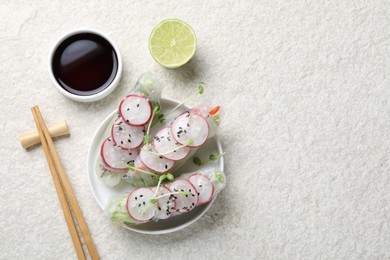 Delicious spring rolls, chopsticks, soy sauce and lime on light grey table, flat lay. Space for text