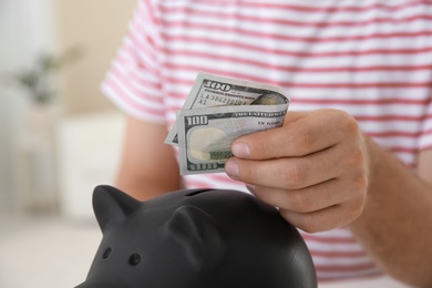 Photo of Man putting money into piggy bank on blurred background, closeup