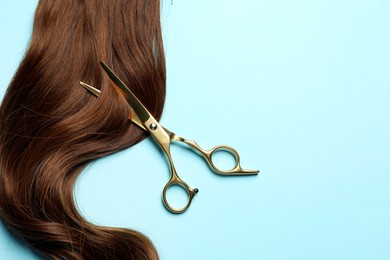 Professional hairdresser scissors with brown hair strand on light blue background, top view. Space for text