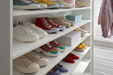 Photo of White shelving unit with collection of colorful sneakers indoors