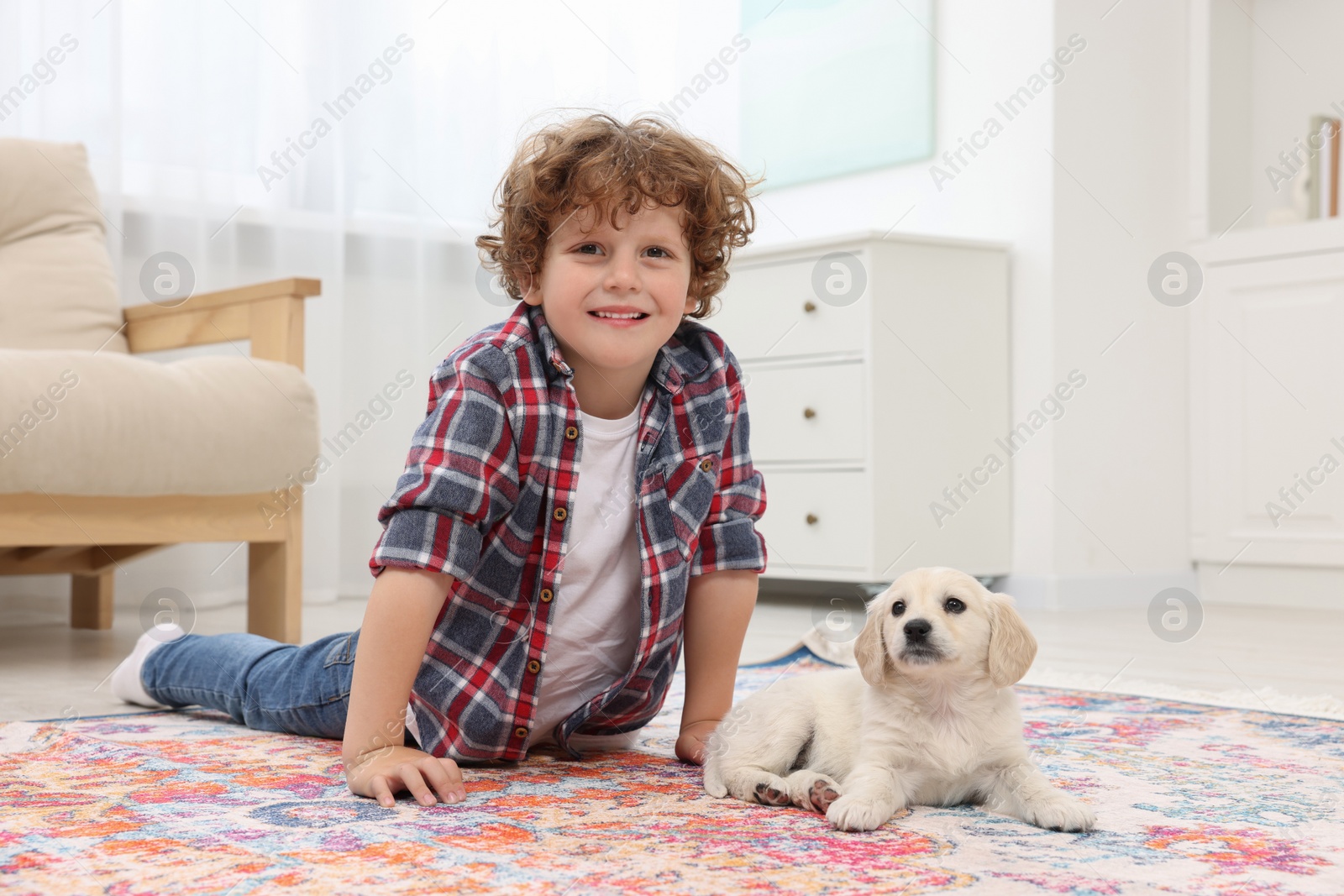 Photo of Little boy lying with cute puppy on carpet at home