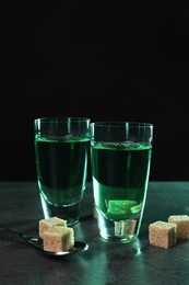 Photo of Tasty absinthe drink in shot glasses and spoon with brown sugar cubes on grey table