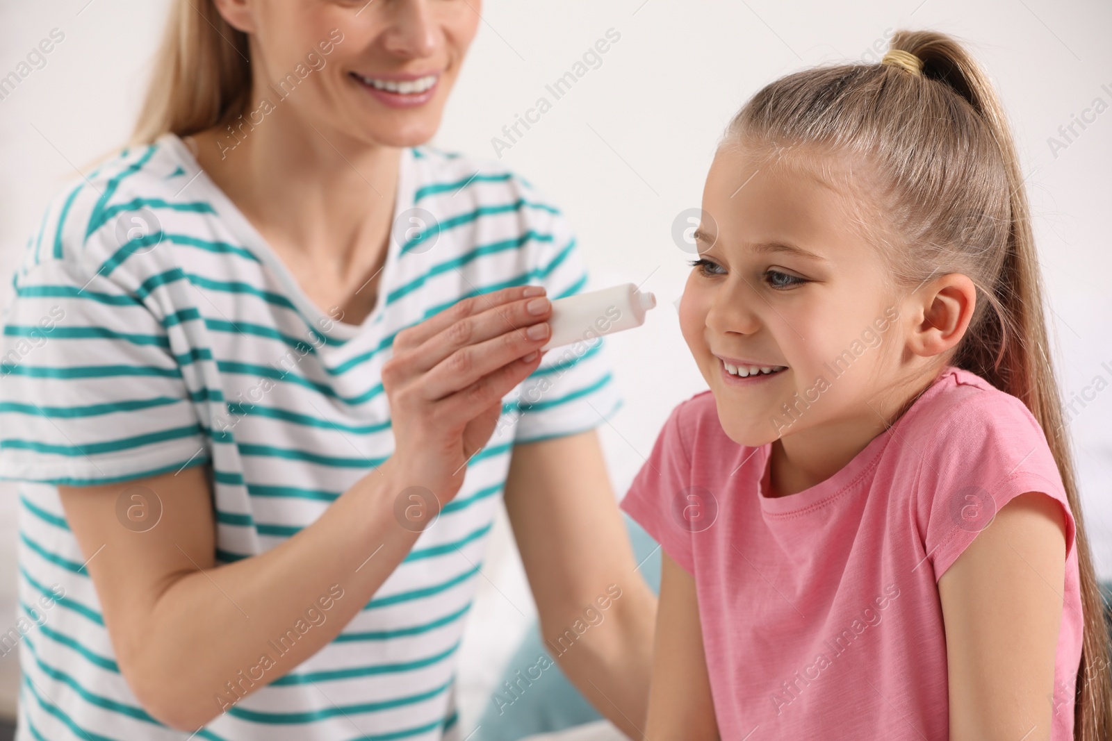 Photo of Mother applying ointment onto her daughter's cheek on white background