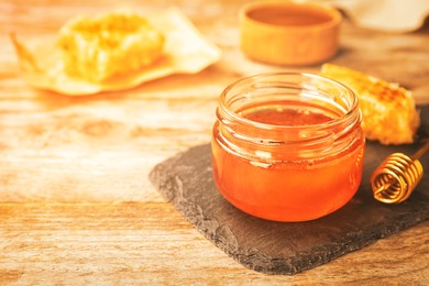 Image of Glass jar with sweet honey and dipper on wooden table, closeup. Space for text