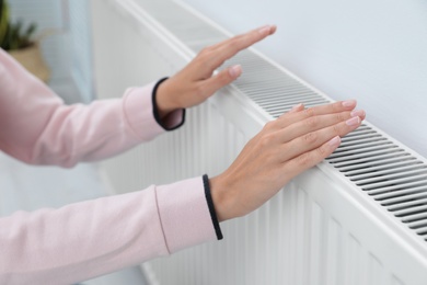 Photo of Woman warming hands on heating radiator near white wall, closeup