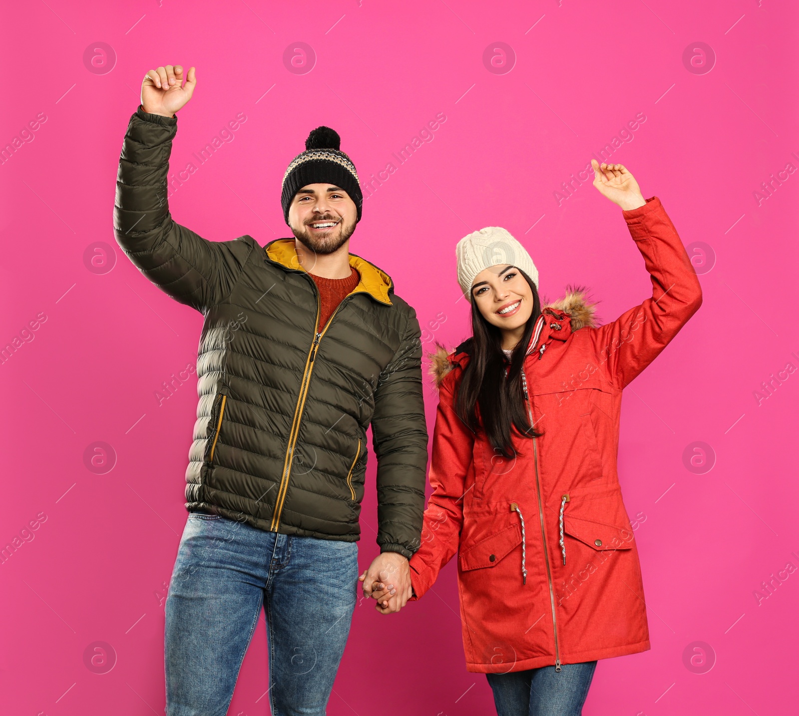 Photo of Happy young couple in warm clothes on pink background. Winter vacation