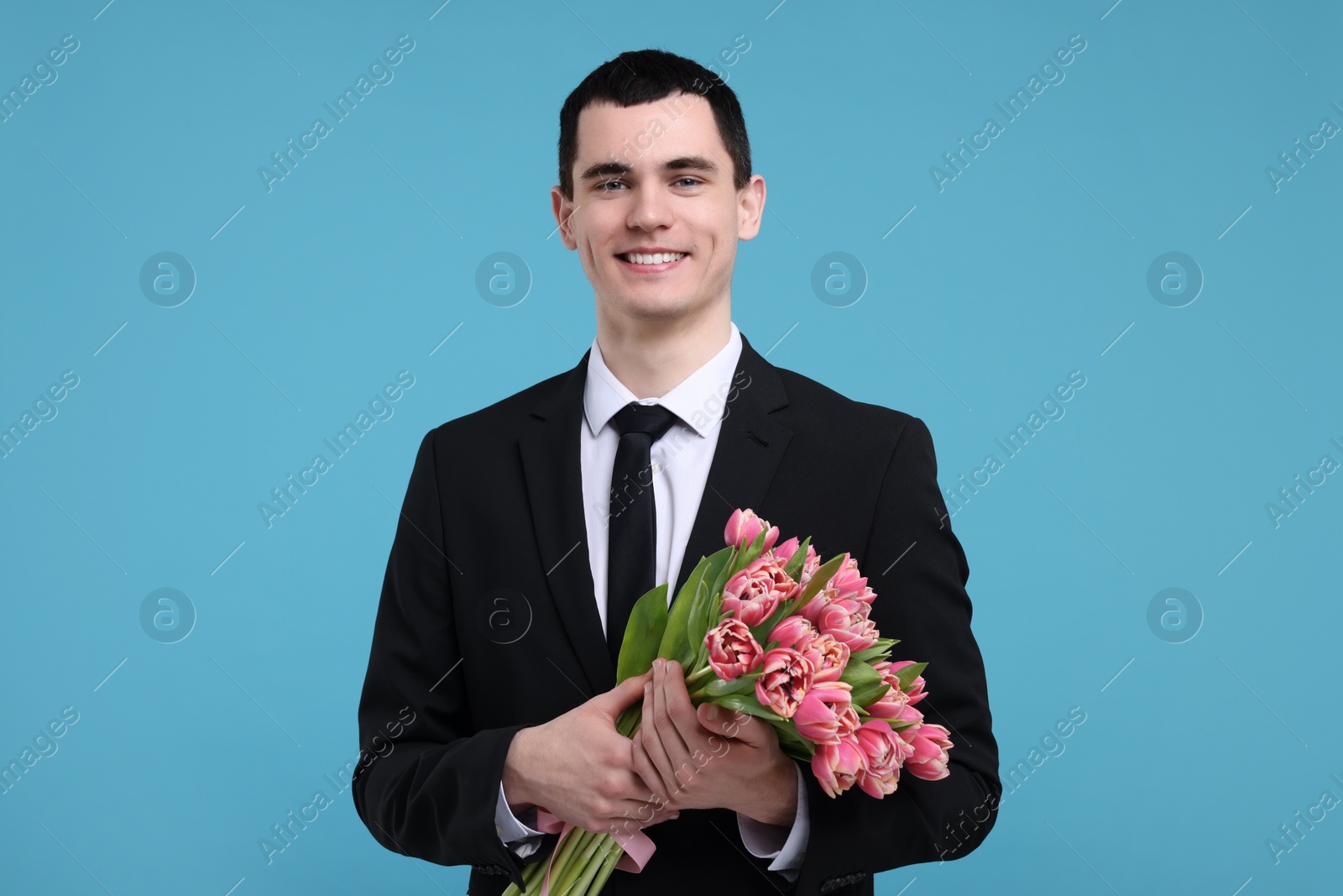 Photo of Happy young man with beautiful bouquet on light blue background