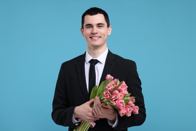 Photo of Happy young man with beautiful bouquet on light blue background