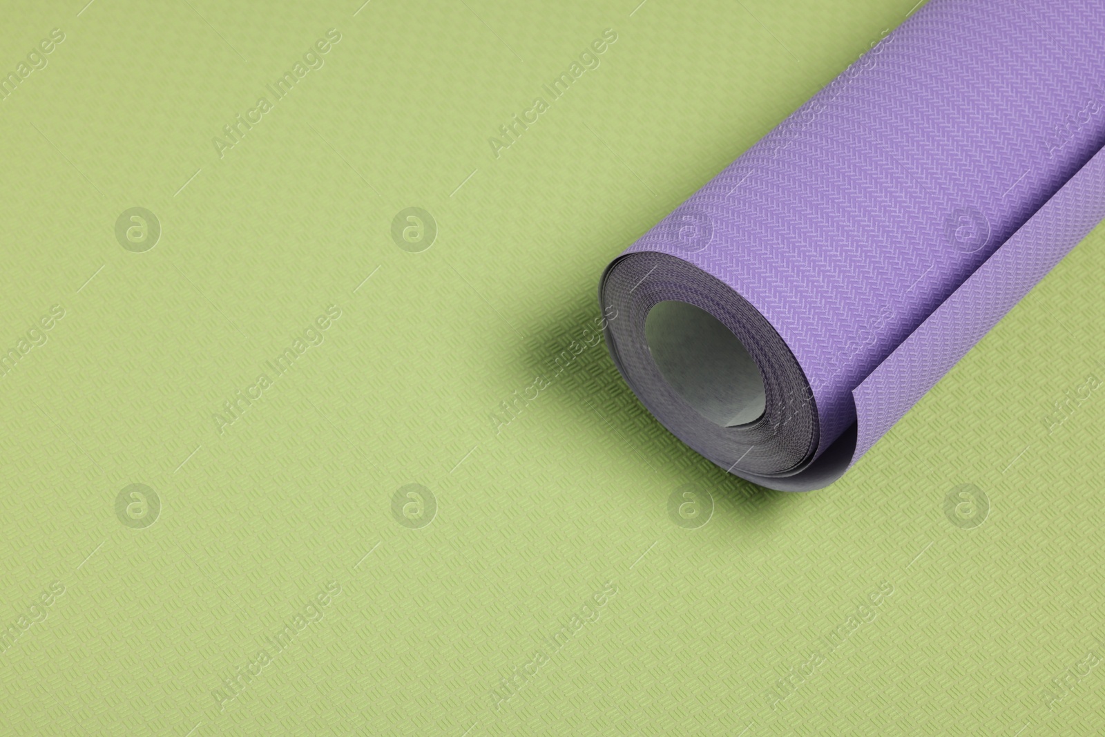 Photo of One violet wallpaper roll on green sample, space for text