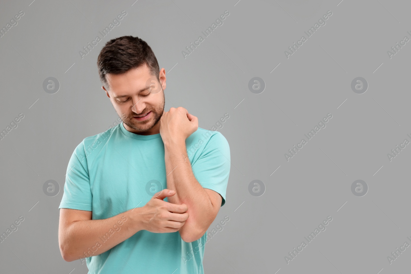 Photo of Allergy symptom. Man scratching his arm on light grey background. Space for text