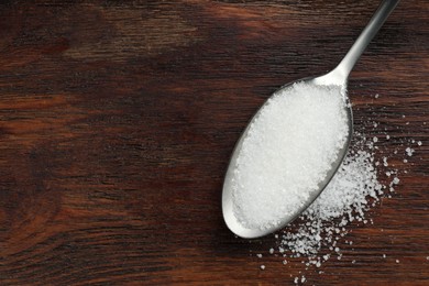 Photo of Spoon with granulated sugar on wooden table, top view. Space for text