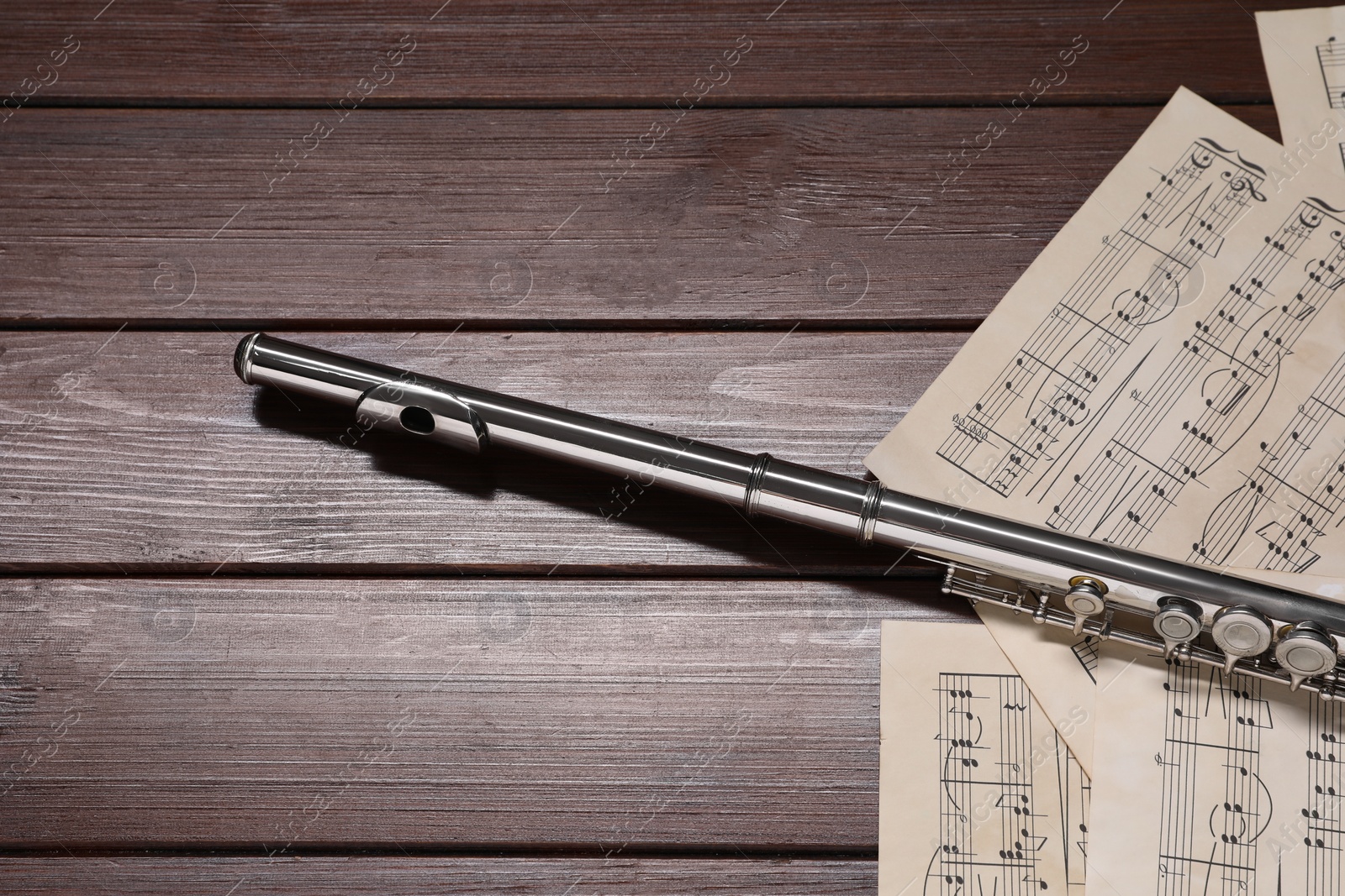 Photo of Sheets with musical notes and flute on wooden table. Space for text