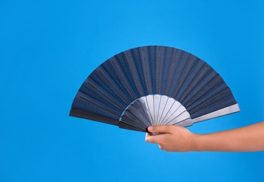 Woman holding black hand fan on light blue  background, closeup