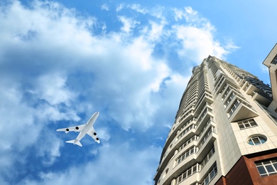 Image of Airplane flying in blue sky over skyscraper