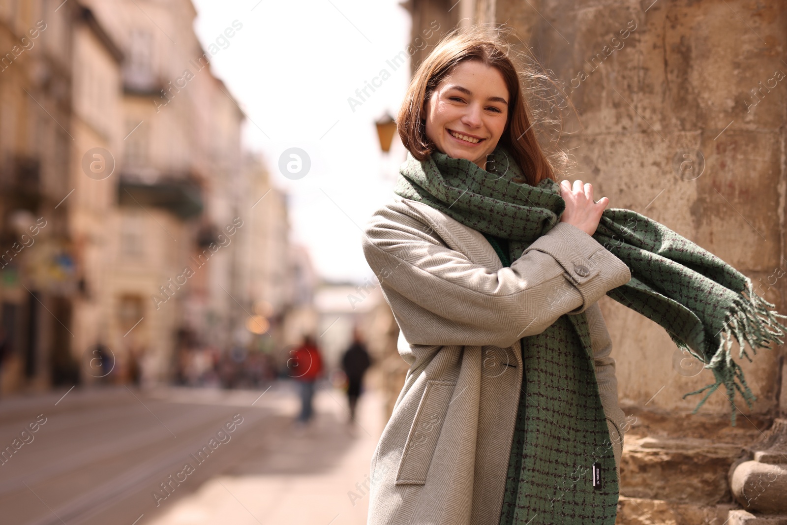 Photo of Beautiful woman in warm scarf on city street, space for text