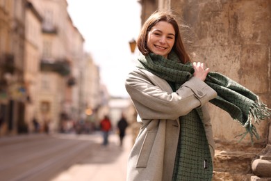 Photo of Beautiful woman in warm scarf on city street, space for text