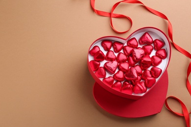 Box of heart shaped chocolate candies and ribbon on brown background, flat lay. Space for text