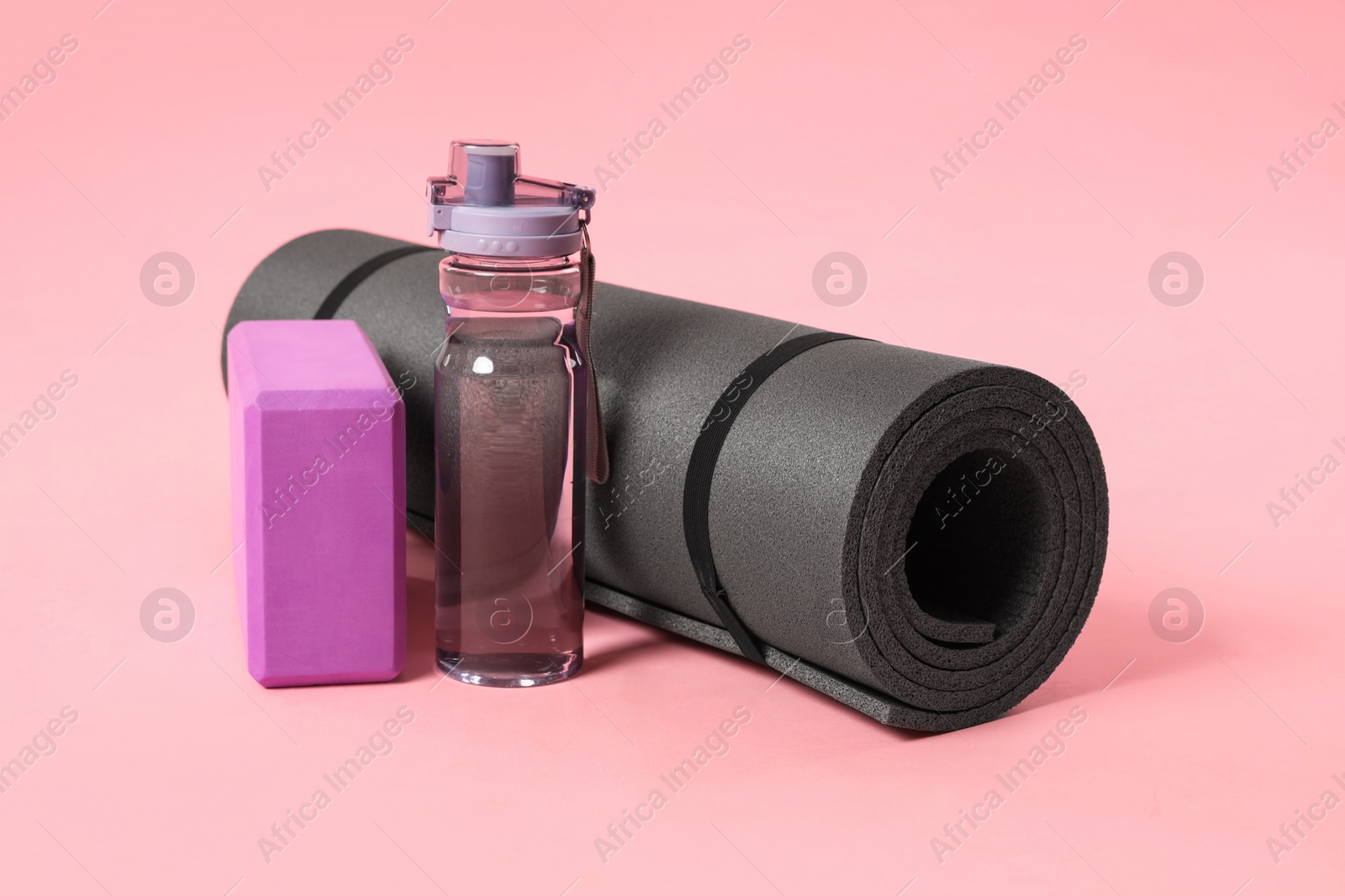 Photo of Grey exercise mat, yoga block and bottle of water on pink background