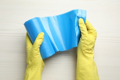 Janitor in rubber gloves holding roll of light blue garbage bags over white wooden table, top view