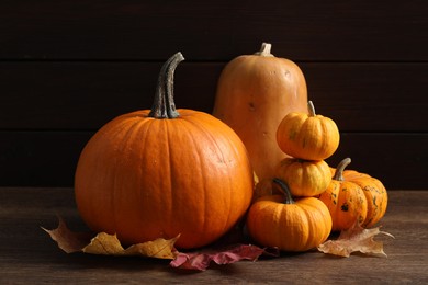 Photo of Thanksgiving day. Pumpkins and leaves on wooden table, closeup