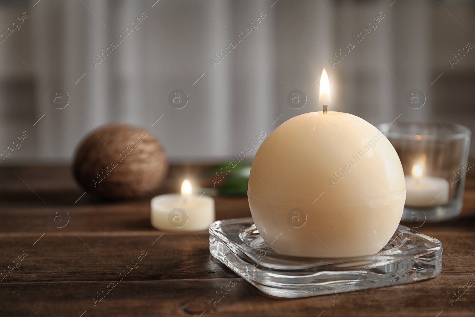 Photo of Glass stand with burning wax candle on wooden table