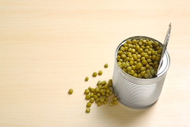 Open tin can of green peas on wooden table, space for text