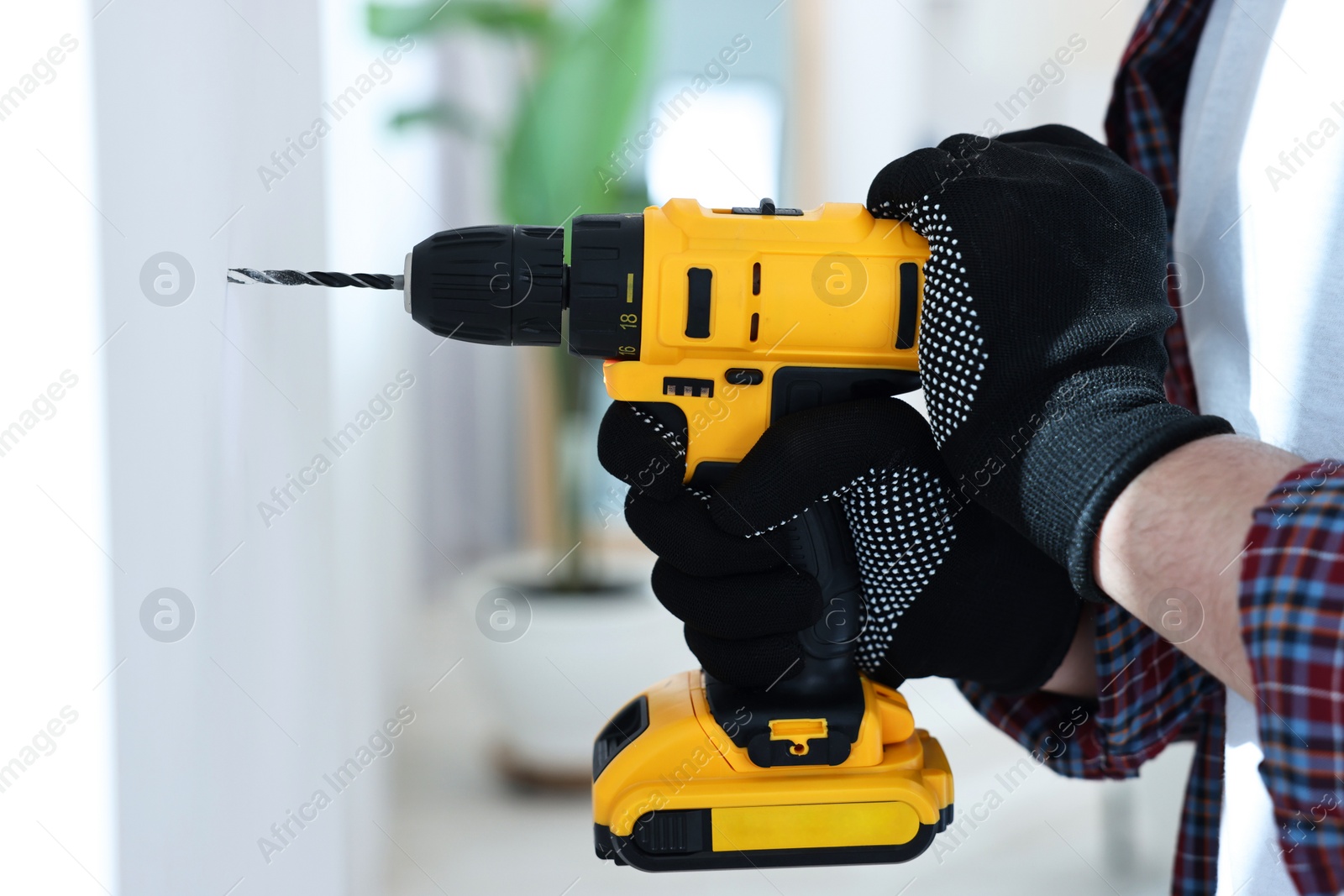 Photo of Young handyman working with electric drill at home, closeup