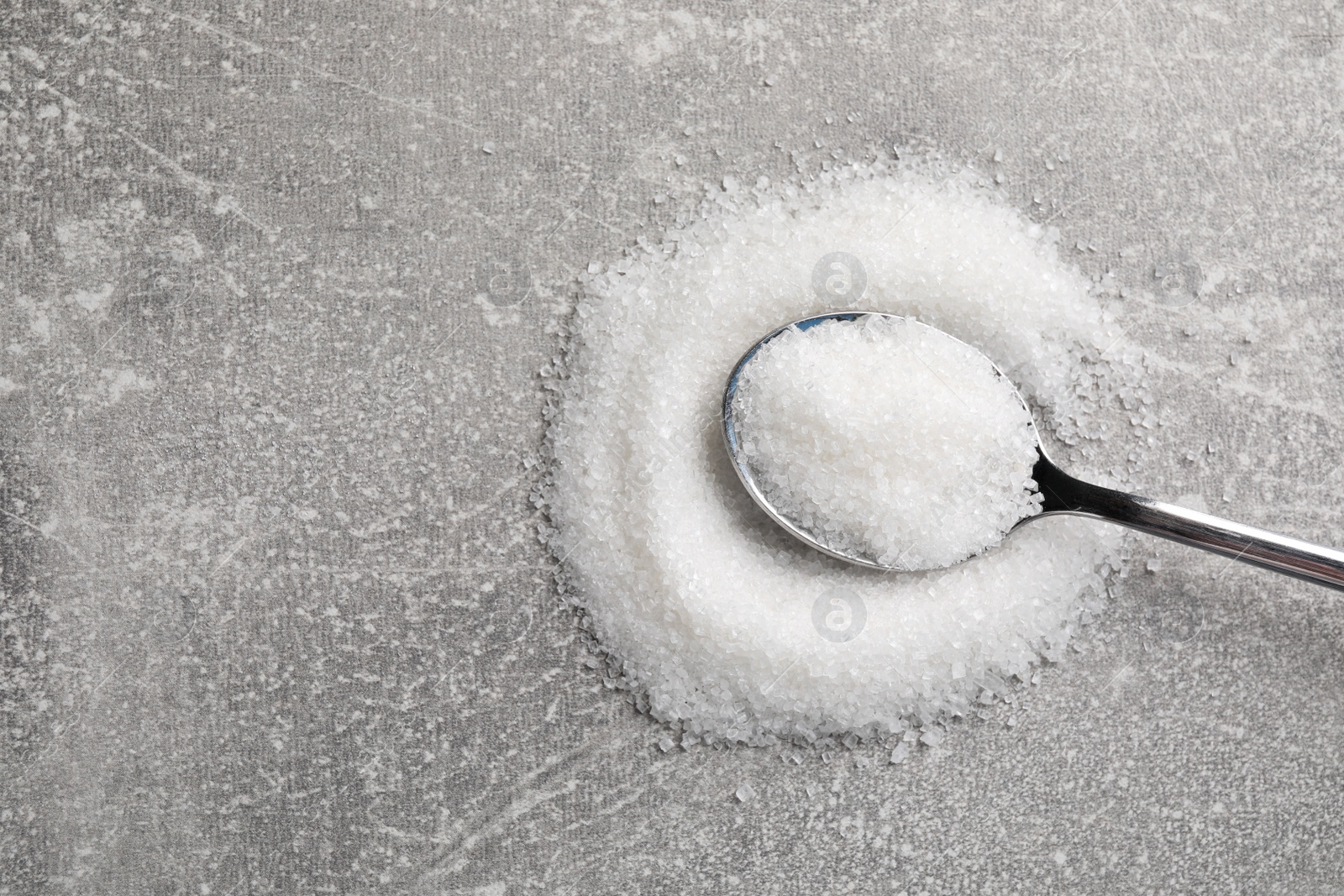 Photo of Granulated sugar and spoon on light grey table, top view. Space for text