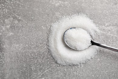 Photo of Granulated sugar and spoon on light grey table, top view. Space for text