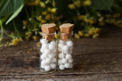 Photo of Bottles with homeopathic remedy on wooden table near flowers, closeup