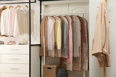 Photo of Garment bags with clothes on rack in dressing room