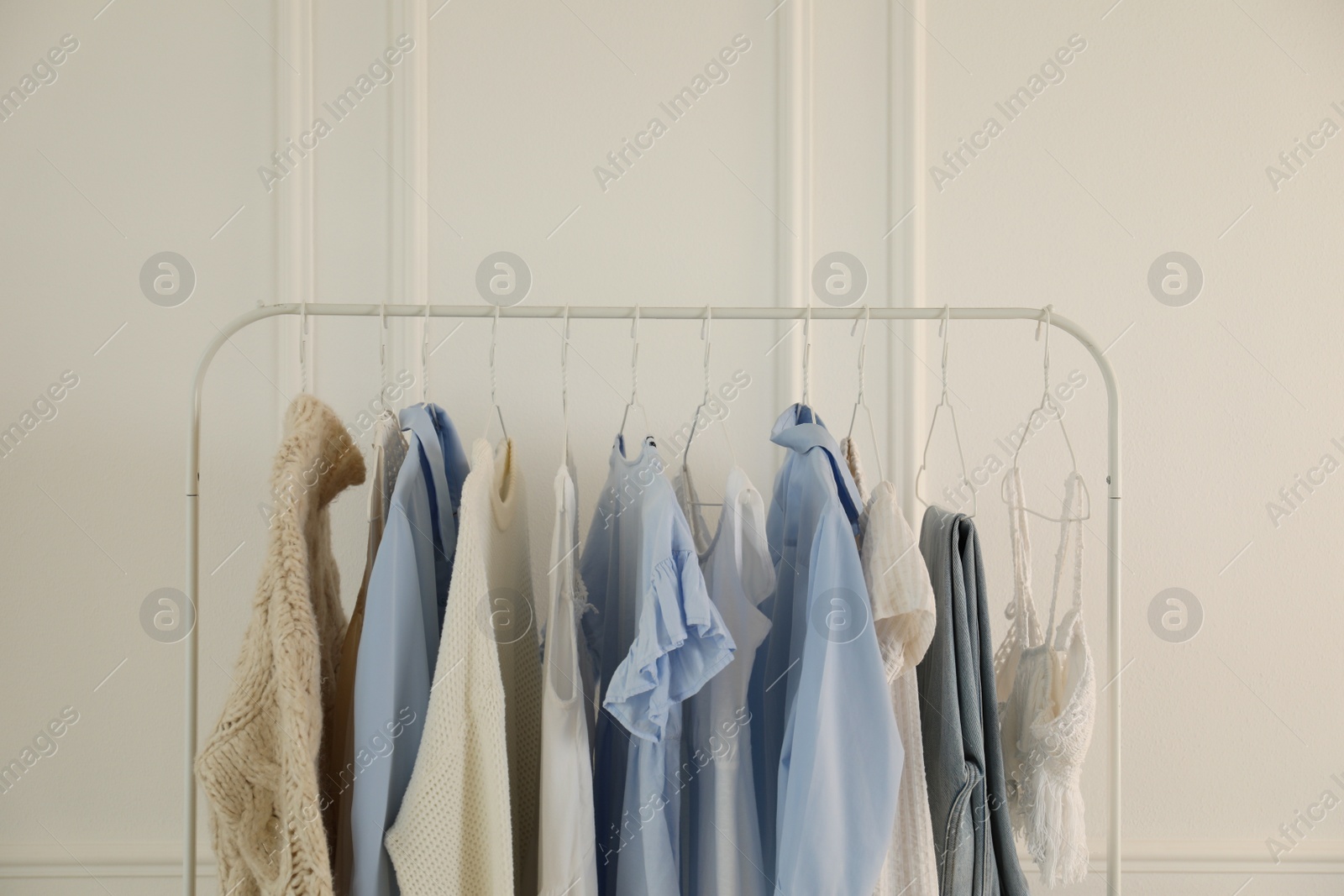 Photo of Rack with stylish women's clothes near white wall. Interior design
