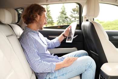 Photo of Attractive young man with tablet on backseat in luxury car