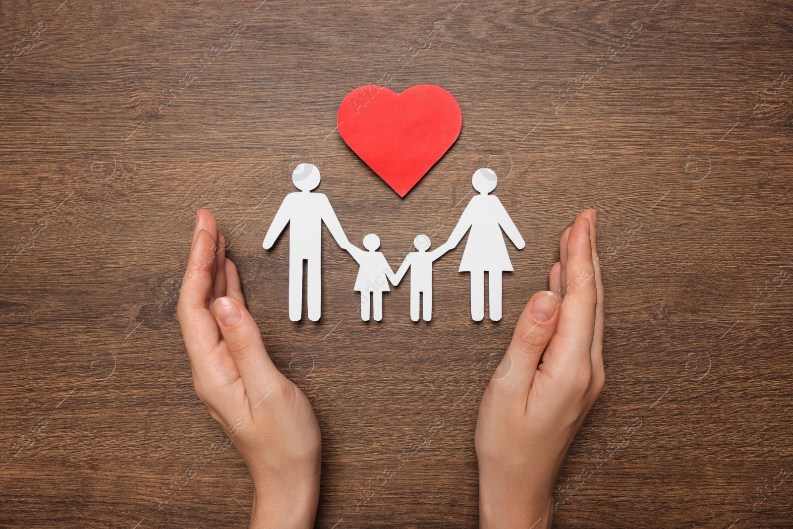 Photo of Woman protecting paper family cutout at wooden table, top view. Insurance concept