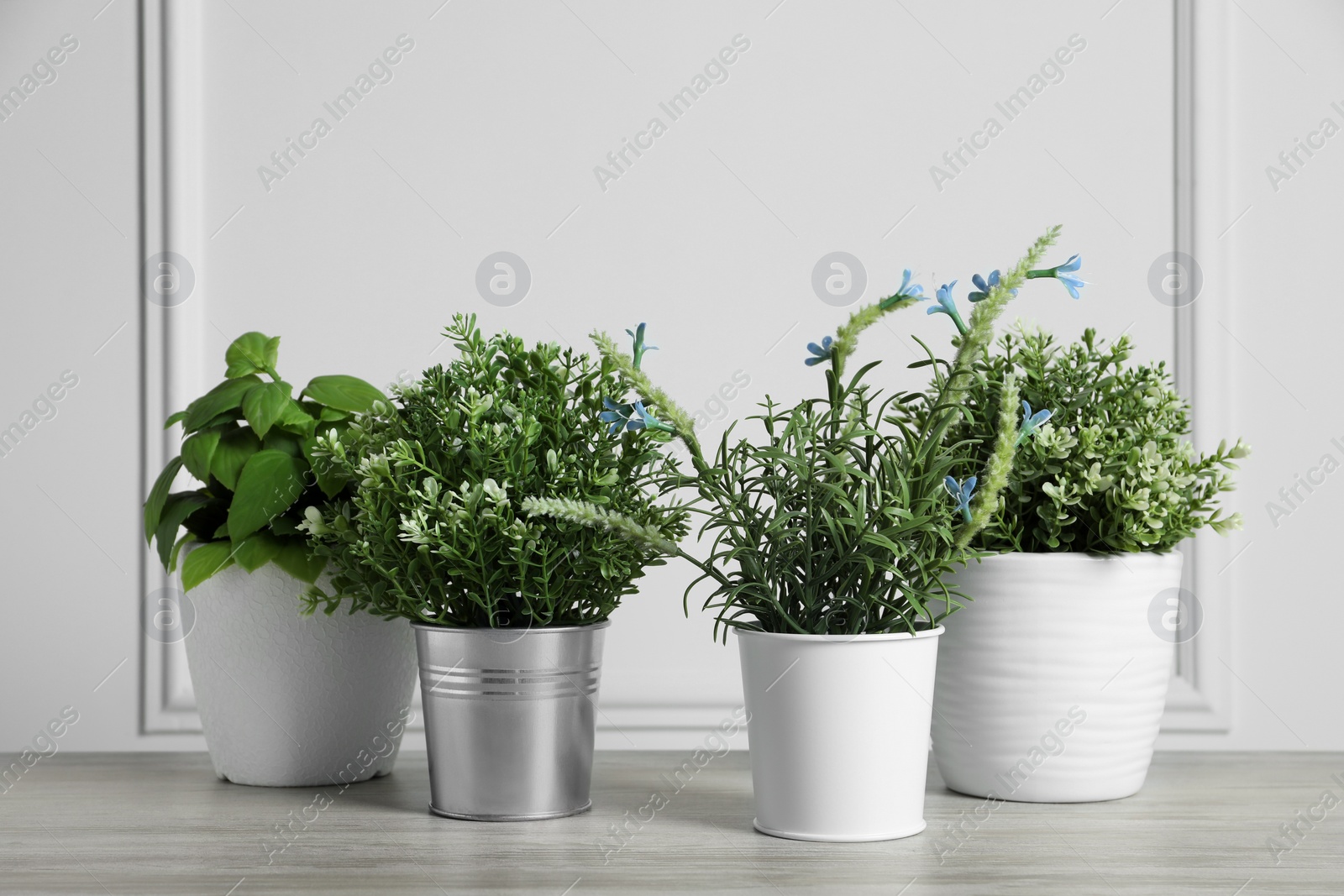 Photo of Different artificial potted herbs on wooden table near white wall
