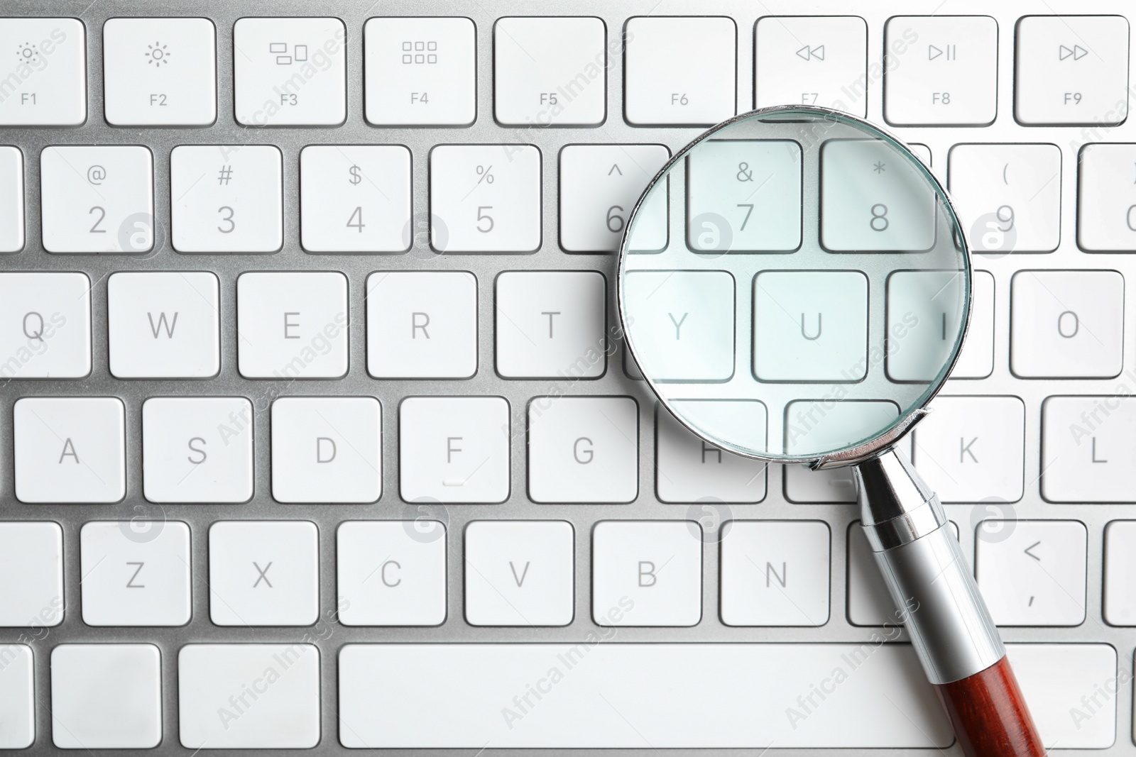 Photo of Magnifier glass on modern keyboard, top view. Find keywords concept